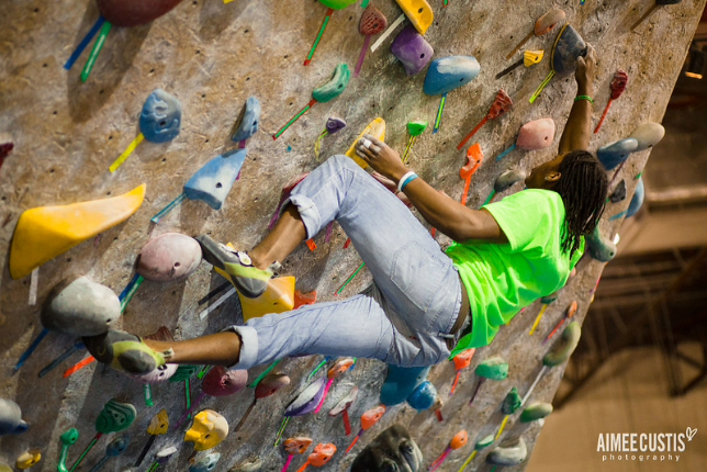 Climber at an indoor boulering gym, reaching up as they climb on an overhang.